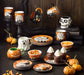 Halloween-themed tableware including mugs, plates, and bowls with decorative designs on a dark surface.