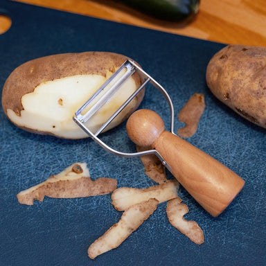 Peeler with a peeled potato on a blue cutting board