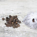 Spices including black peppercorns and star anise on a light surface with a white mesh bag.