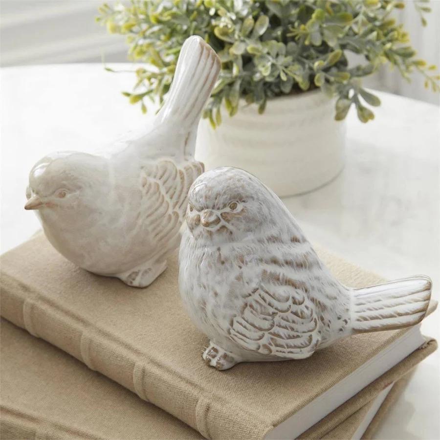 Two white ceramic birds on a beige book with a plant in the background