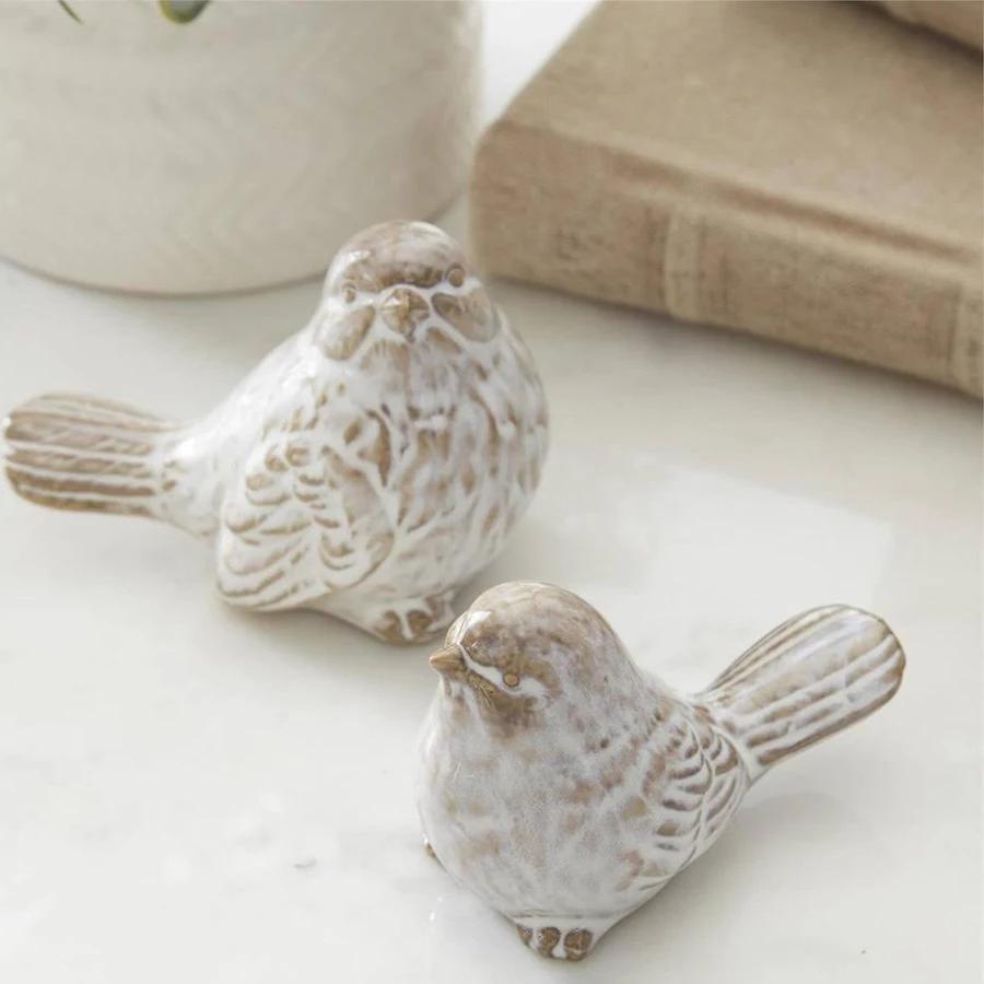 Two ceramic bird figurines on a light surface with a blurred background