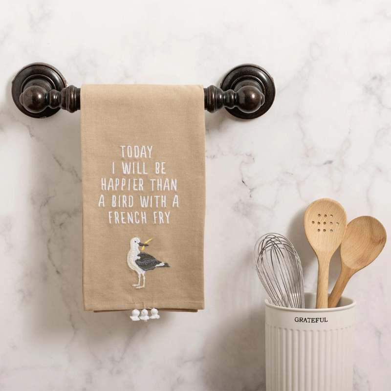 Kitchen towel with motivational quote hanging on a rack, next to wooden utensils in a container.