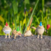 Five small frog figurines with colorful hats and a red balloon on a stone surface with a green leafy background.