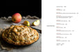 Apple pie on a wooden table with apples and a book open to a recipe page.