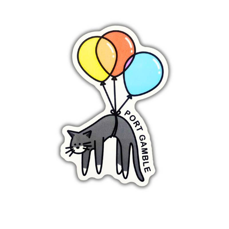 A die-cut sticker featuring a cartoon gray cat carrying three balloons in yellow, orange, and light blue, with the text 'PORT GAMBLE' printed along the right side, shown on a plain white background.