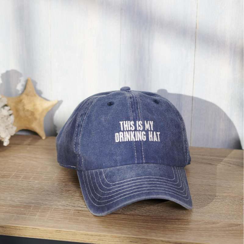 Blue cap with 'This is my drinking hat' text on a wooden surface