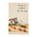 Beach scene with a small house and text 'home is a place by the sea' on a beige background