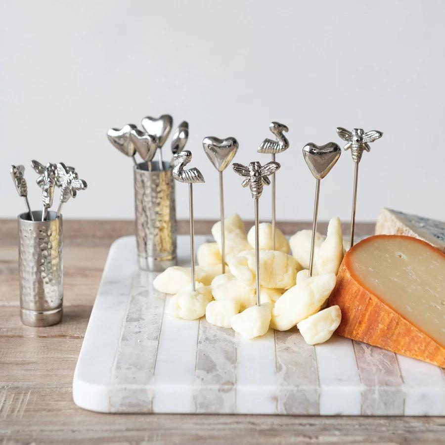 Metal skewers with heart and animal designs on a marble board with cheese.