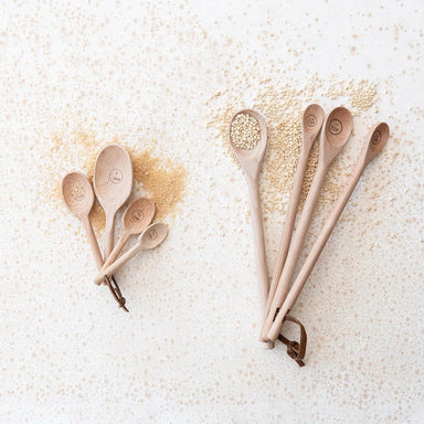 Set of wooden spoons with a small pile of quinoa on a light background