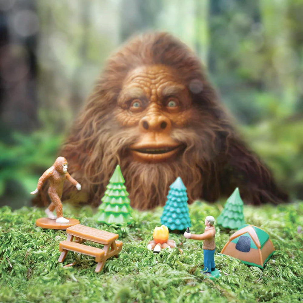 Sasquatch-like creature interacting with a miniature campsite in a forest setting.