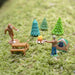 Miniature figures of a person, a tent, a picnic table, and trees on a grassy surface.