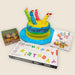 Colorful birthday cake with candles, 'Happy Birthday' string lights box, and party favor bags on a white background.