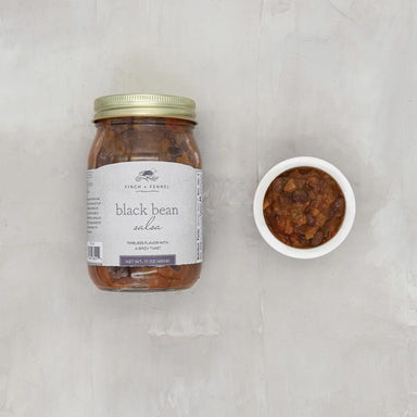 Jar of black bean salsa with a small bowl of salsa on a light gray background