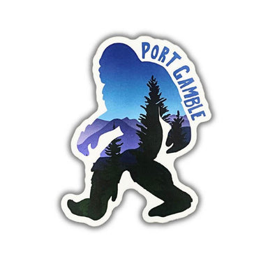A die-cut sticker featuring a Bigfoot silhouette filled with a blue and purple mountain-and-trees landscape, with the words “PORT GAMBLE” in blue arched over the top, shown on a plain white background.