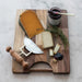Wooden cutting board with cheese, a knife, and a jar of jam on a marble surface