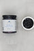 Jar of 'Blueberry Lemon Thyme' preserve with a small dish of the preserve on a gray background