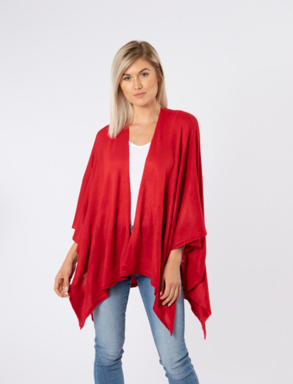 Woman wearing a red poncho over a white top and blue jeans on a light gray background