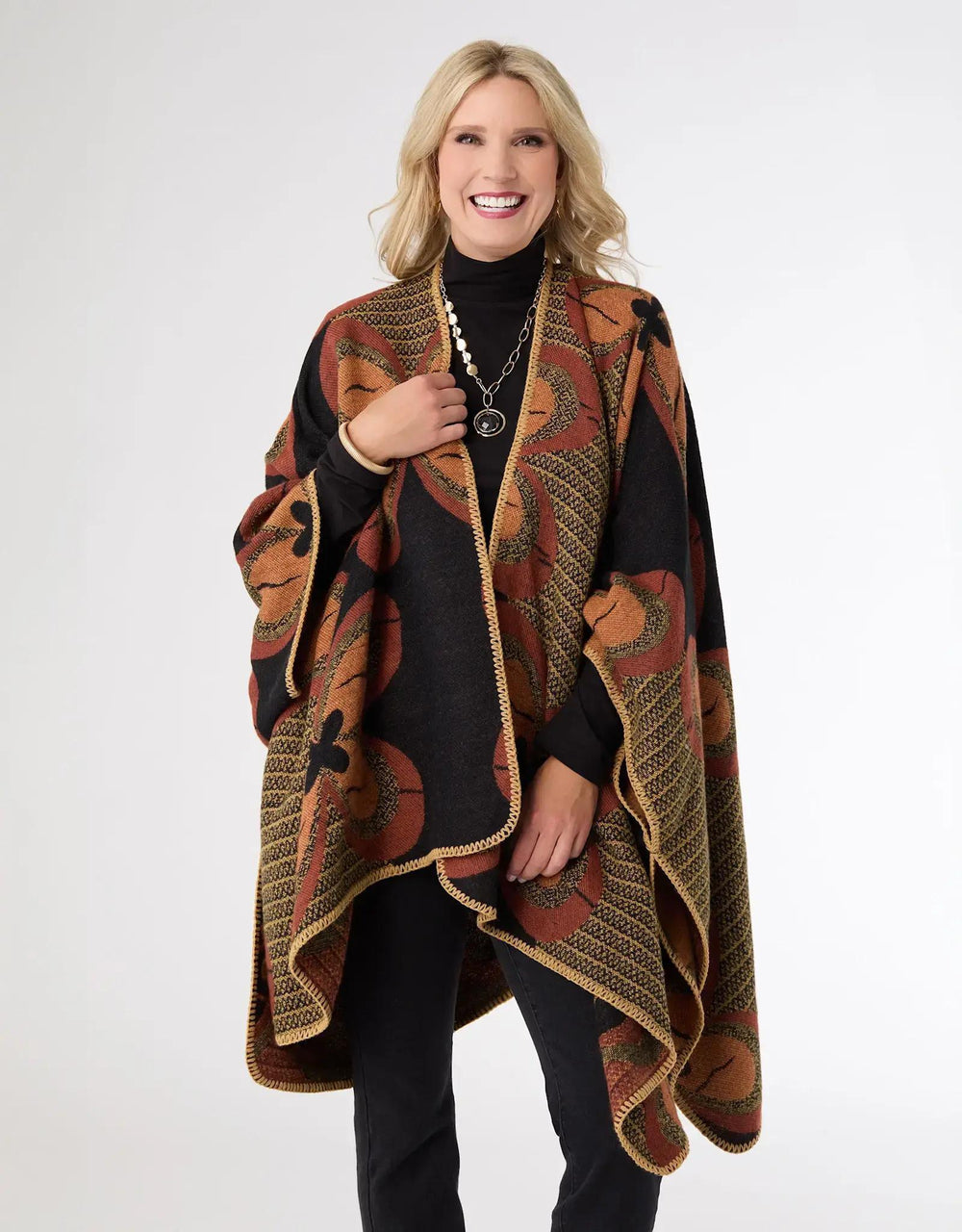 Woman wearing a patterned poncho over a black outfit on a white background