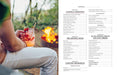 Person holding a cocktail by a campfire with a menu on the right side.