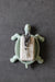 Tortoise-shaped soap holder with a bar of soap and lavender on a dark gray background