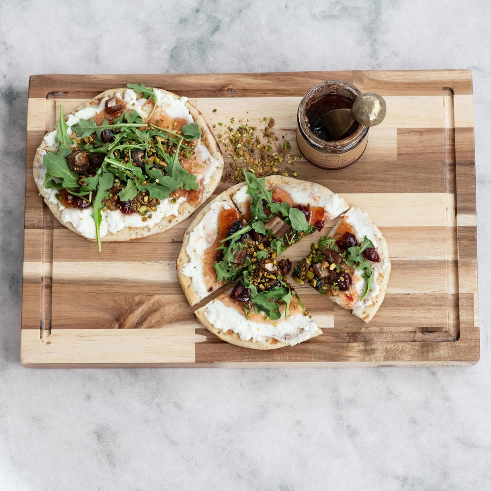 Two small pizzas with arugula and toppings on a wooden cutting board.