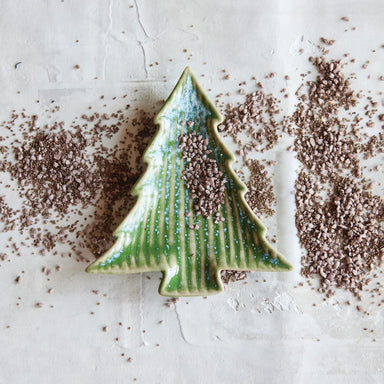 Ceramic Christmas tree ornament on a textured surface with brown specks