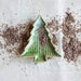 Ceramic Christmas tree ornament on a textured surface with brown specks