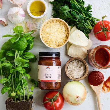 Ingredients for pizza making including herbs, tomatoes, cheese, and sauce on a white surface.