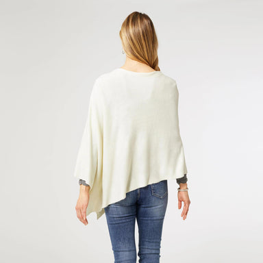 Woman wearing a cream poncho and blue jeans on a white background