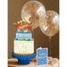 Birthday cake with colorful decorations, balloons, and a card on a brown background