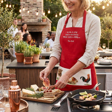Woman in a red apron cooking outdoors with friends in the background