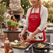 Woman in a red apron cooking outdoors with friends in the background