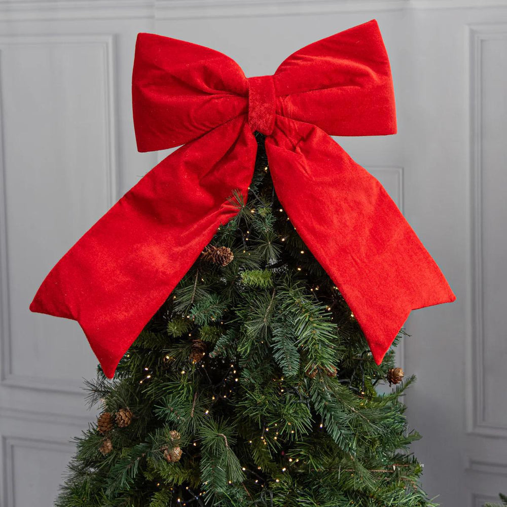 Christmas tree with a large red bow against a gray wall