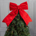 Christmas tree with a large red bow against a gray wall