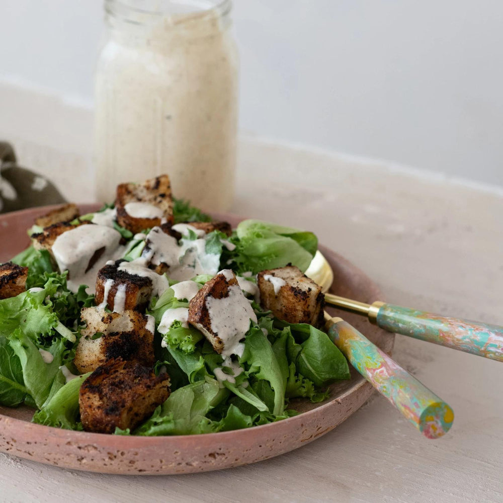 Salad with croutons and a creamy dressing on a plate with a fork, set against a neutral background.