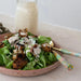 Salad with croutons and a creamy dressing on a plate with a fork, set against a neutral background.