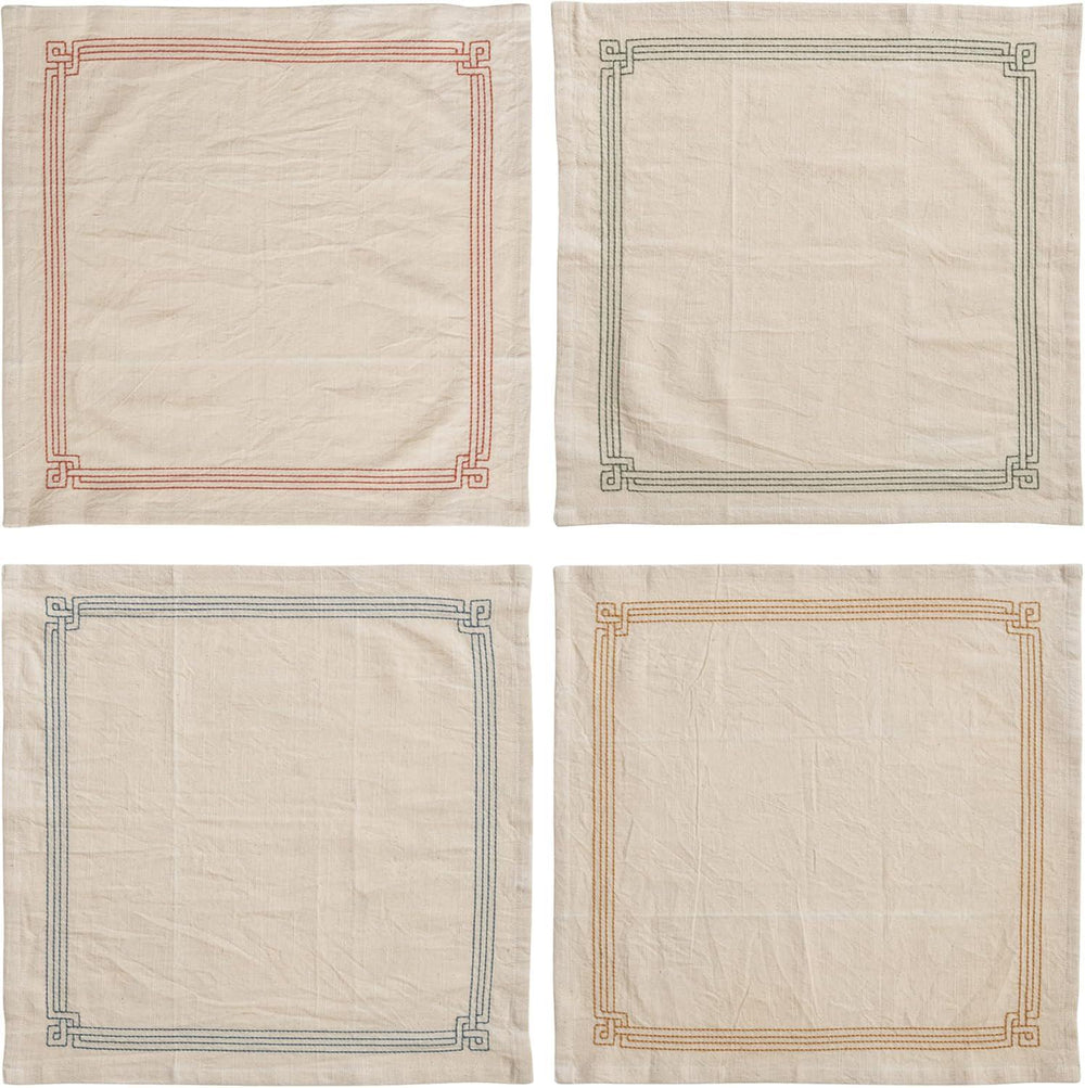 Four beige napkins with embroidered borders on a white background
