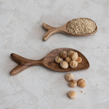 Two wooden spoons with seeds on a light gray surface
