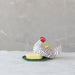Decorative chicken-shaped object with a small plate on a textured surface