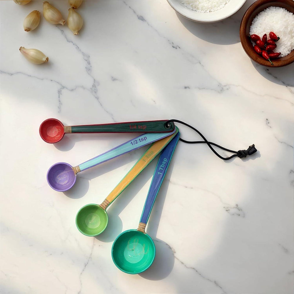Set of colorful measuring spoons on a marble surface with small bowls of spices.