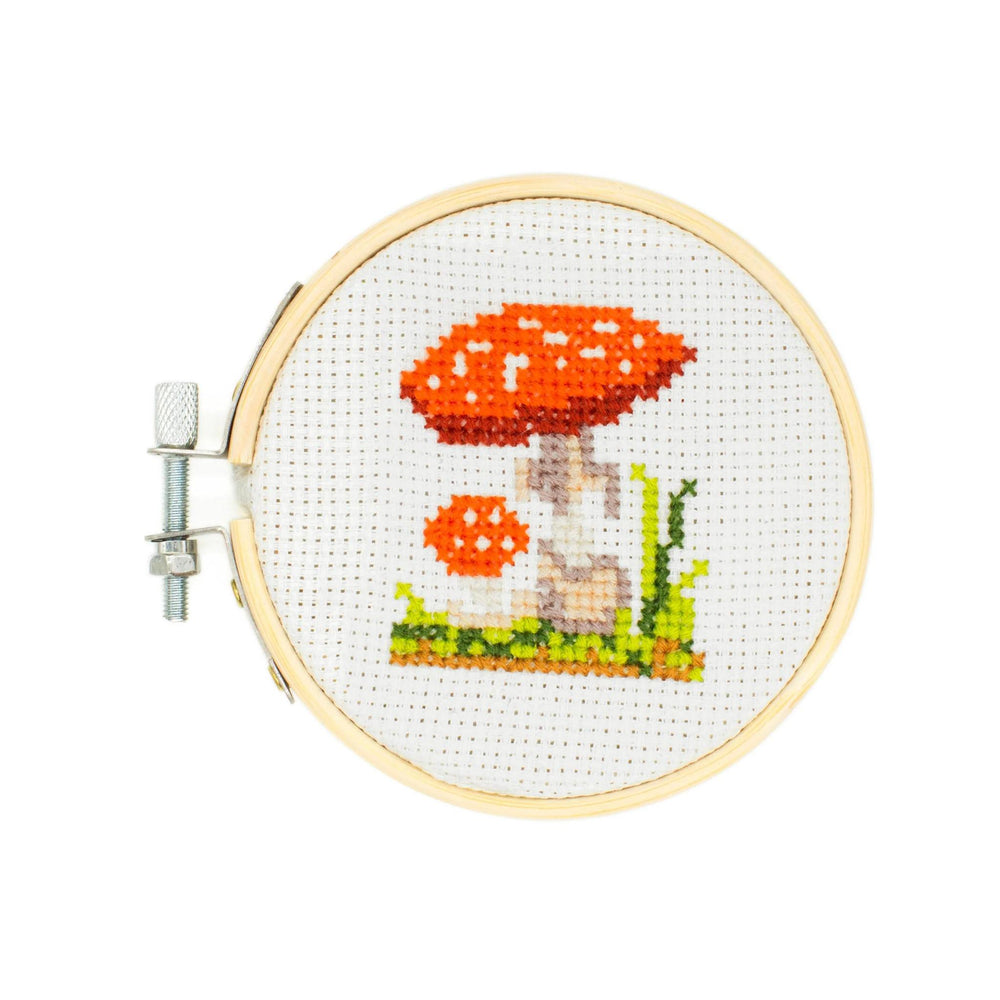 Cross-stitched mushroom design in a wooden hoop on a white background