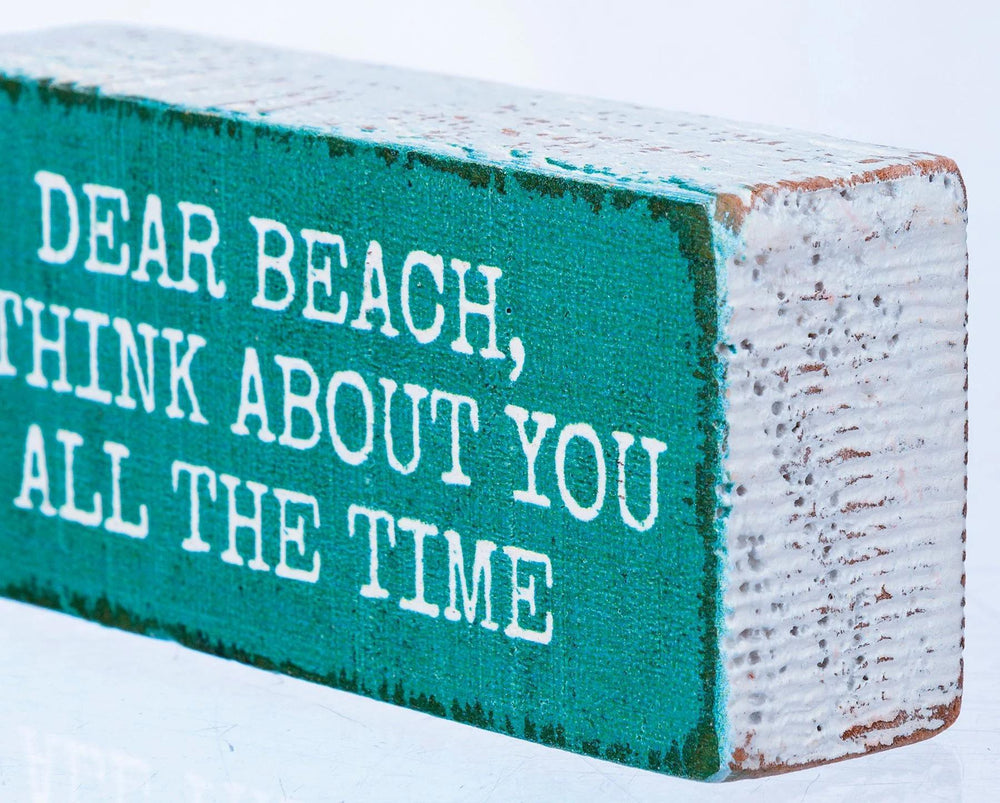 Wooden block with text 'Dear Beach, think about you all the time' on a snowy background