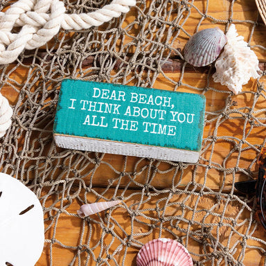 Small turquoise sign with text on a wooden surface with seashells and fishing net