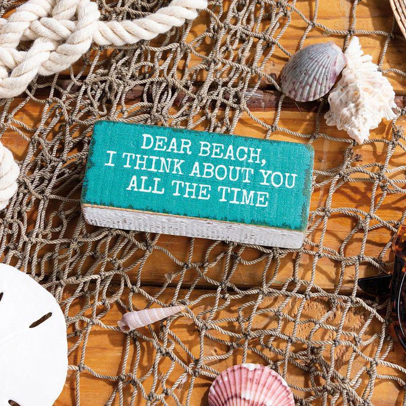Small turquoise sign with text on a wooden surface with shells and netting