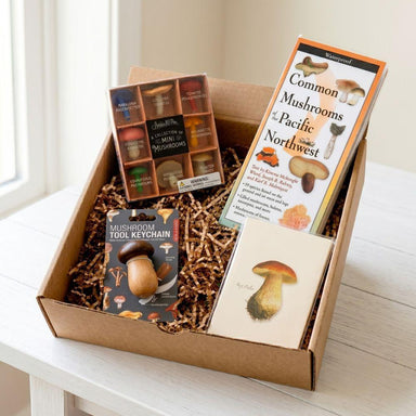 Mushroom-themed gift box with books, keychain, and cards on a white surface.