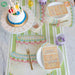 Children's birthday party setup with a small cake, plates, and napkins on a table.