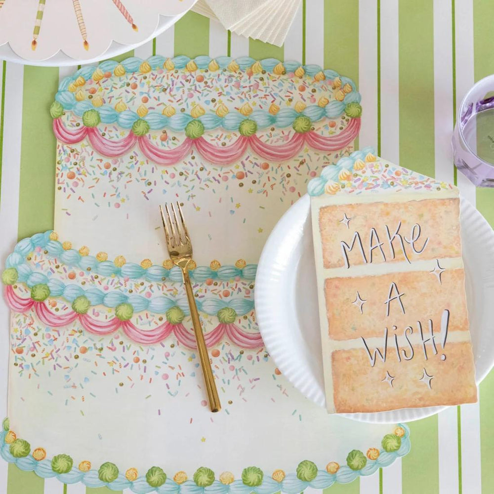 Decorative table setting with a cake-shaped napkin, fork, and 'Make a Wish!' card on a striped background.