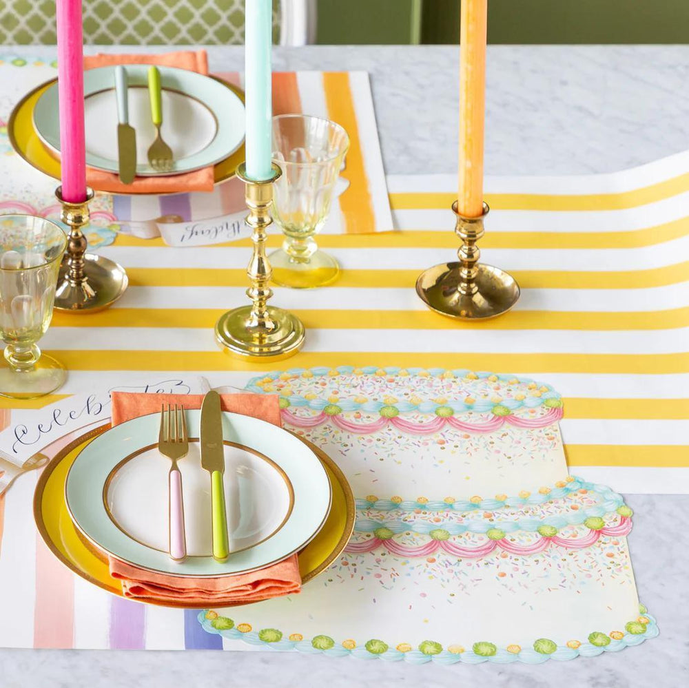 Colorful table setting with striped tablecloth, plates, cutlery, and candles.