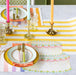 Colorful table setting with striped tablecloth, plates, cutlery, and candles.