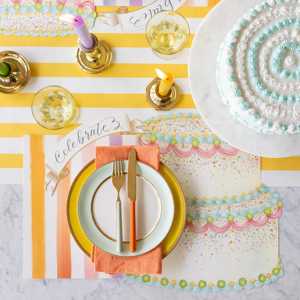 Colorful table setting with a cake, place cards, and cutlery on a striped tablecloth.